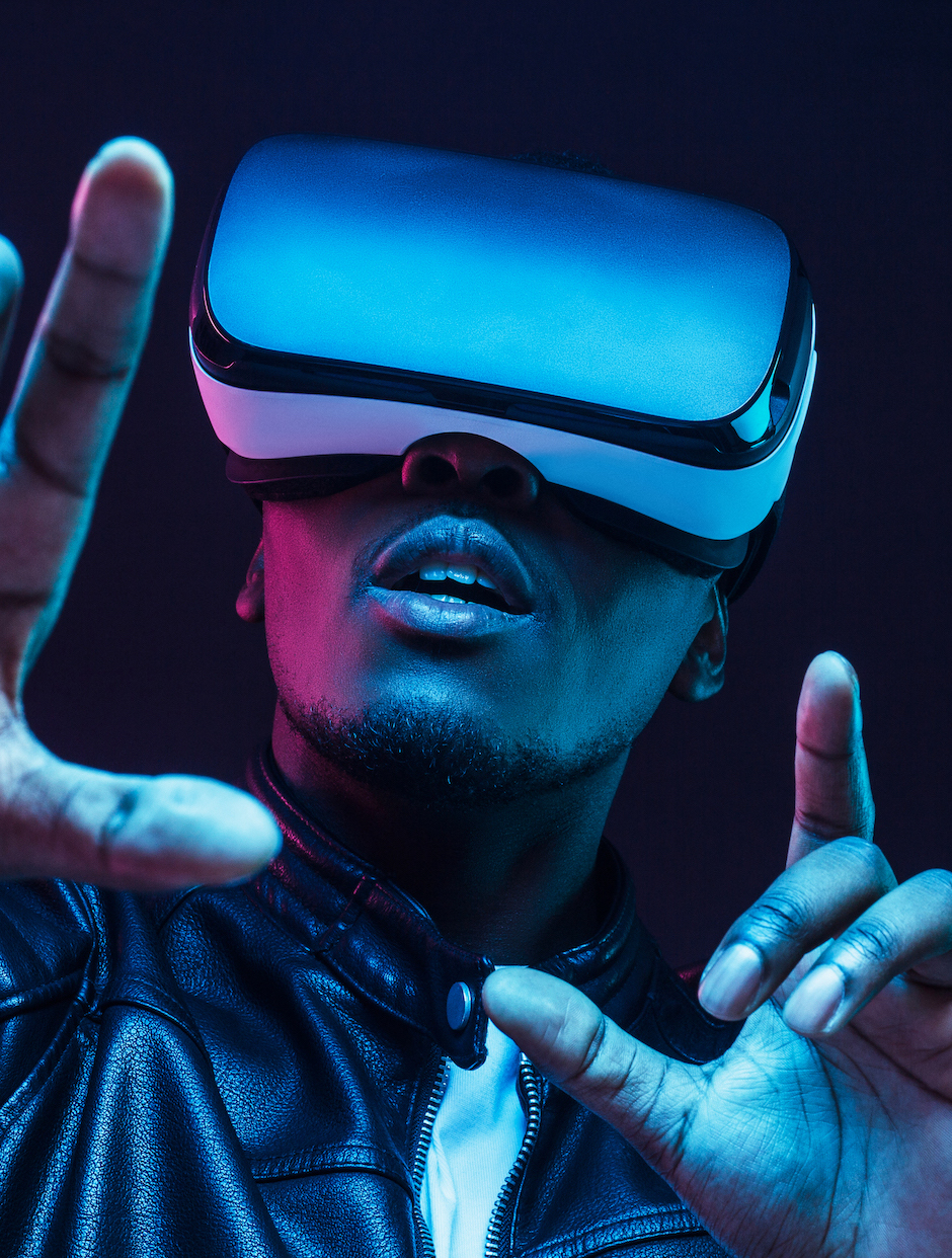 Young african man wearing virtual reality goggles with hands up, isolated on black background